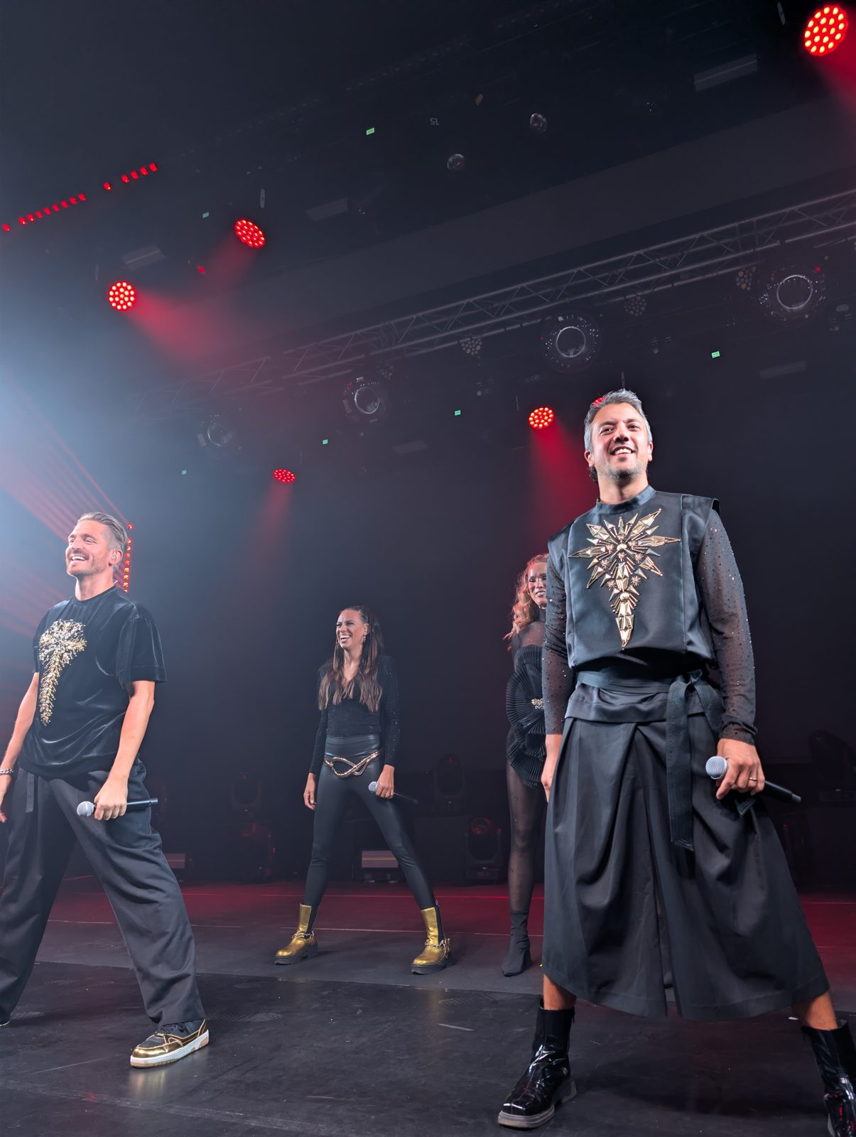 All four A*Teens members performing together under red stage lights in Mexico City, 2025