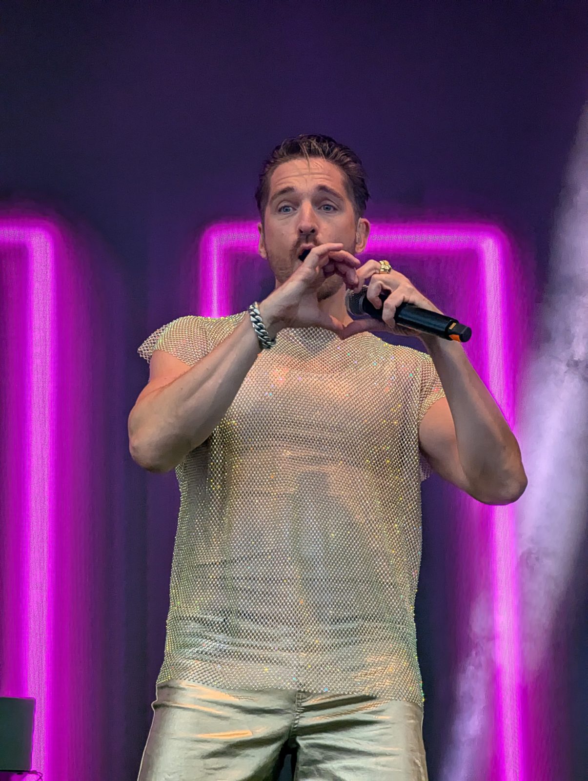 A*Teens member making a heart shape with the microphone under purple neon lighting in Oslo, 2025