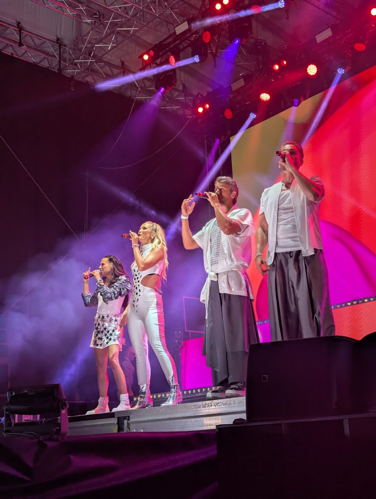 All four A*Teens members performing together under purple stage lighting in Stockholm, 2025